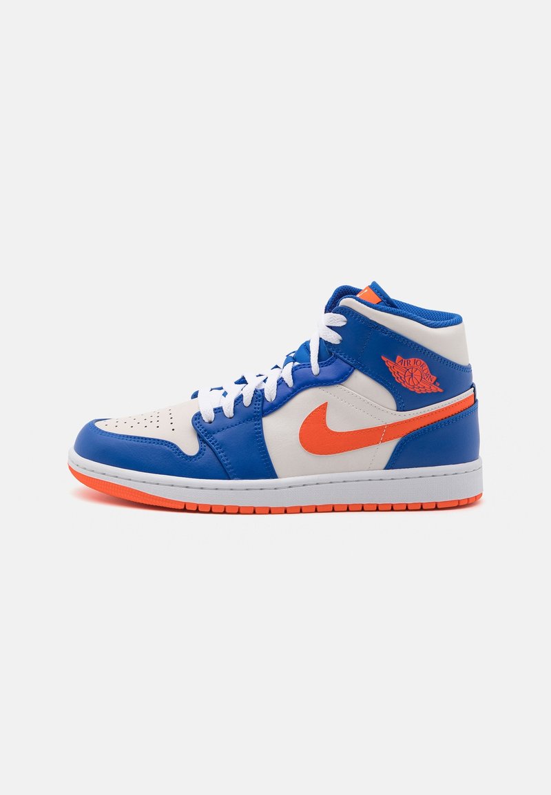 Sneaker montante en cuir blanc et bleu avec un swoosh Nike orange vif, un logo Air Jordan wings, des lacets blancs et une semelle orange.