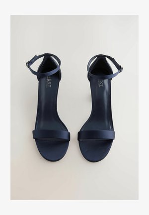 Mornarsko plave sandale na petu otvorene s sjajnom satenskom završnom obradom, tanke vezice oko gležnja i širokom prednjom trakom. Moderna, minimalistička izrada. Gumeni potplat.