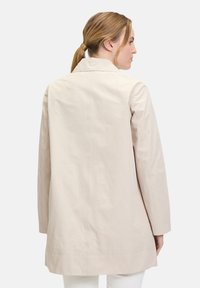 Beige leichter Mantel mit einem Kragen, langen Ärmeln und geradem Schnitt, der über eine glatte Textur und saubere Nähdetails verfügt.