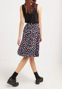 Rozšířená sukně do půli kol v námořnické barvě s bílými a červenými abstraktními vzory, vyrobená z lehké látky. V kombinaci s černými kotníkovými botami.