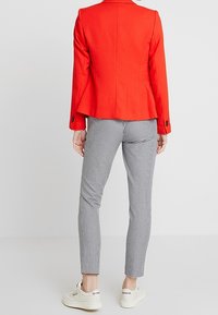 Punainen räätälöity bleiseri mustilla napeilla, yhdistetty mustavalkoisiin ruutuhousuihin ja valkoisiin lenkkareihin. Sileä pinta ja istuva muotoilu.