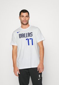 Hvid bomulds t-shirt med "DALLAS" og "77" i marineblå og blå. Har Nike-logoen på venstre skulder, rund halsudskæring og korte ærmer.