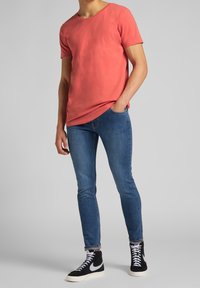 Camiseta de algodón coral de manga corta con cuello redondo, combinada con unos vaqueros ajustados azules y zapatillas negras de caña alta con detalles en blanco.