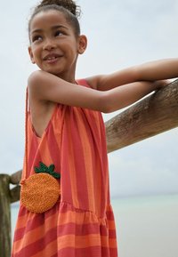 Vestito a strisce rosse e arancioni con gonna arricciata. Presenta una borsa arancione decorata con perline e dettagli in foglia verde. Ringhiera in legno sullo sfondo.