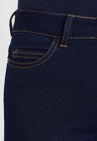 Mörkblå denimjeans med smal passform, orange sömmar och en klassisk design med framfickor. Tyget är slätt med lätt stretch.