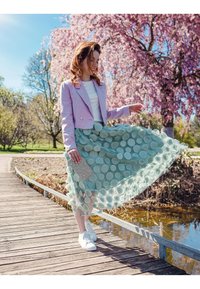 Light pink cropped jacket, white top, and a mint green skirt with circular embellishments. White sneakers and a textured gray clutch.