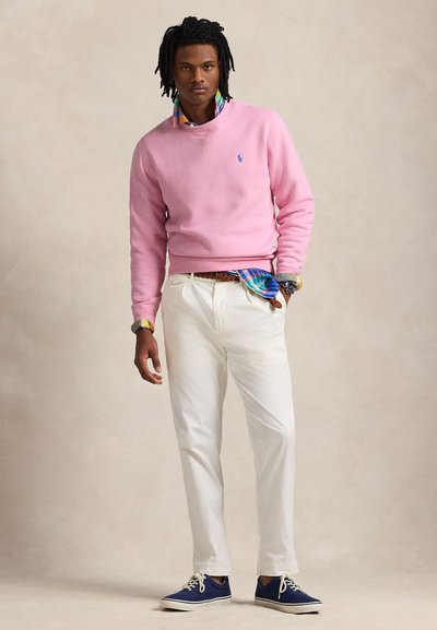 Sweatshirt cor-de-rosa, calças brancas, ténis azuis. Gola de camisa aos quadrados com padrão multicolorido e cinto visível por baixo do sweatshirt.