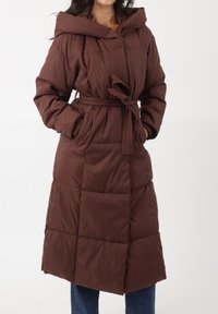 Bruine gewatteerde jas met capuchon, tailleceintuur en grote zakken. Heeft een doorgestikt ontwerp en een middellange lengte voor extra warmte.