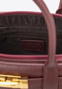 Wnętrze brązowej torby na ramię z wieloma zasuwanymi kieszeniami, teksturowaną podszewką i skórzaną metką z wytłoczonym nazwiskiem marki. Złote akcenty sprzętowe.