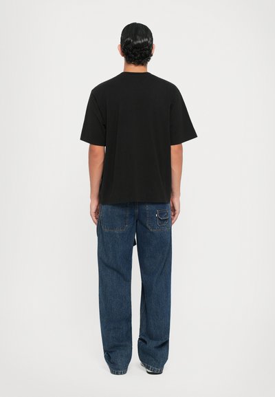 Camiseta negra de manga corta hecha de algodón, combinada con unos vaqueros de mezclilla azul de corte holgado que cuentan con un bolsillo trasero y un acabado desvanecido.