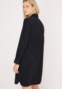 Langärmliges, dunkelblaues Kleid aus Cord-Stoff. Mit einem Kragen und Knopfmanschetten, sowie einem leicht abgerundeten Saum.