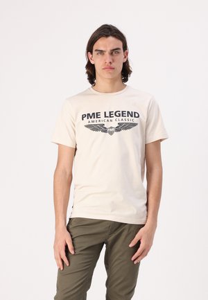 T-shirt en coton beige avec un imprimé marine portant "PME LEGEND AMERICAN CLASSIC" et un graphique d'aigle. Encolure ronde, manches courtes, design ajusté.