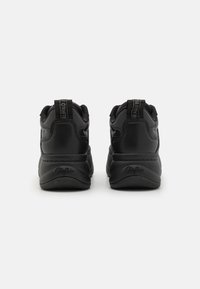 Svarta sneakers med en slät syntetisk ovandel, vadderad krage och kontrasterande varumärkesdragremmar bak. Texturerad sula för grepp.