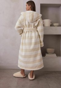 Vit och beige randig morgonrock med huood och bälte, tillverkad av mjukt fleece-material. Matchas med fluffiga tofflor på ett kaklat golv.