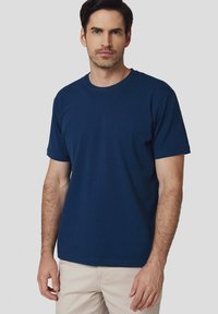 Granatowa bawełniana koszulka z okrągłym dekoltem, krótkimi rękawami i luźnym krojem. Materiał wydaje się gładki z minimalną ilością szwów i detali.