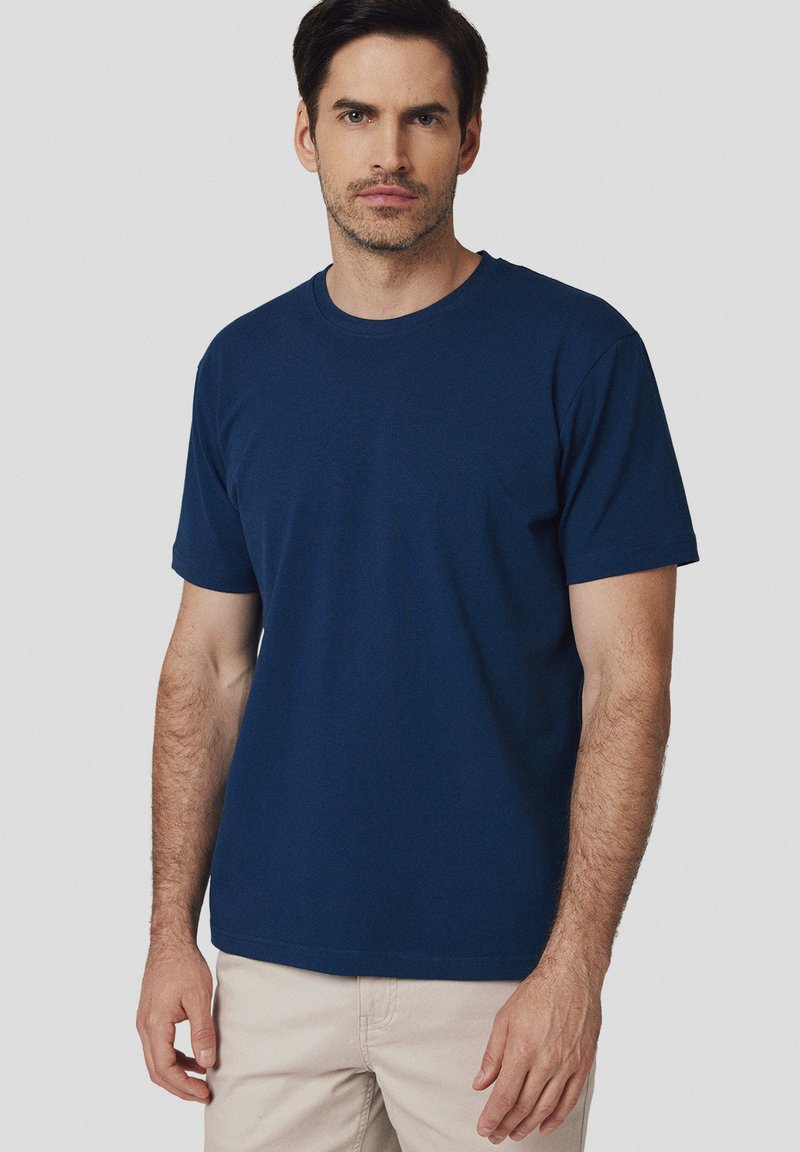 Granatowa bawełniana koszulka z okrągłym dekoltem, krótkimi rękawami i luźnym krojem. Materiał wydaje się gładki z minimalną ilością szwów i detali.