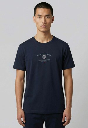 Jeune homme de face portant un t-shirt bleu marine avec le texte et le logo "Patrouille de France Athos Jet Team" sur la poitrine.