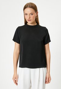 Sort kortærmet top, rund halsudskæring, bl�ød tekstur, afslappet pasform, minimalistisk design, båret med hvide vide bukser, simpel og moderne æstetik.