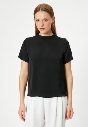 Sort kortærmet top, rund halsudskæring, blød tekstur, afslappet pasform, minimalistisk design, båret med hvide vide bukser, simpel og moderne æstetik.