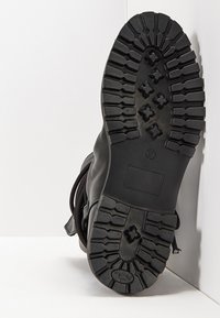Botín de cuero negro con una suela de goma resistente y surcos profundos, diseño de cordones y punta redondeada. El tacón tiene una ligera elevación para proporcionar tracción.