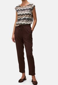Tkaný top s vícero barevným cikcak vzorem, doplněný hnědými kalhotami se stahovací šňůrkou. Boty jsou tmavě hnědé s průstřihovým designem.