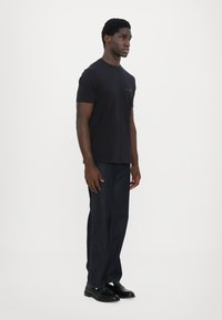 Svart t-skjorte med korte ermer, rund hals, glatt stoff, kombinert med mørkeblå rett ben jeans og svarte lær-sko.