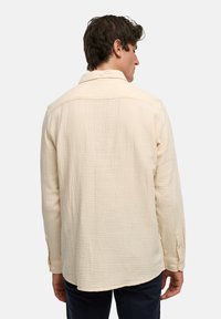 Beige Baumwollhemd mit strukturierter Oberfläche, langen Ärmeln, Knopfverschluss und klassischem Kragen. Der Rücken hat eine Passe und einen abgerundeten Saum.
