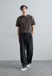 Brown short-sleeve top with a relaxed fit, paired with loose black pants featuring visible stitching and a drawstring waist. White sneakers.
