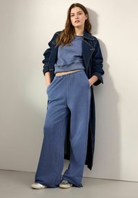 Sweatshirt bleu avec ourlet côtelé et pantalon bleu à jambes larges, tous deux en tissu doux. Associé à un manteau en denim foncé et des baskets argentées.