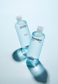 To klare plastikflasker med toner, den ene mærket "DIN HUD ER VORES PLANET" og den anden "Torriden," med en lys blå væske og vanddråber.