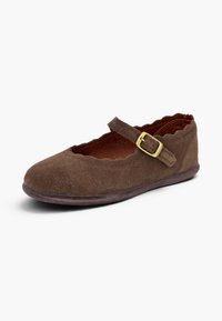 Chaussure Mary Jane en daim marron avec bords festonnés et bride à boucle dorée sur fond blanc.