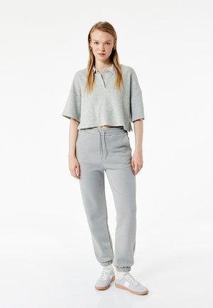 Grå cropped polo shirt med en afslappet pasform, parret med grå joggerbukser med elastisk talje og muffer. Hvide sneakers fuldender looket.