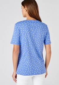 Camiseta azul con lunares hecha de tela suave, con lunares blancos, mangas cortas y un corte relajado, vista por la parte de atrás.