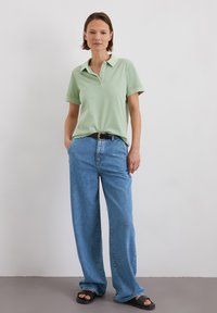 Lichtgroene polo met kraag, gecombineerd met losse blauwe denim jeans en zwarte sandalen. Eenvoudig ontwerp, relaxte pasvorm en effen kleuren.