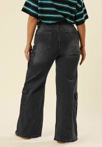 Löysät cargo-housut mustasta denimistä, joissa on sivutaskut, korkea vyötärö ja takataskut. Kangas on haalistuneen näköinen.