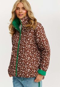 Brązowa puchowa kurtka w wzory z białymi plamkami, z zielonym zamkiem i akcentami kołnierza. Miękka tekstura i pikowana konstrukcja.