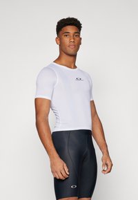 T-shirt de sport blanc à manches courtes avec texture en maille, associé à un short de cyclisme noir moulant. Présente un petit logo sur la poitrine.
