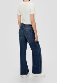 Niebieskie spodnie dzwony o ciemnym odcieniu denimu, z dwoma tylnymi kieszeniami i wysokim stanem. Połączone z teksturowanym białym topem z krótkim rękawem.