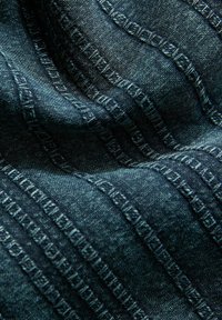 Tissu en denim d'un bleu profond avec des motifs texturés et des lignes de couture en relief. Surface douce, flexible et légèrement lustrée.