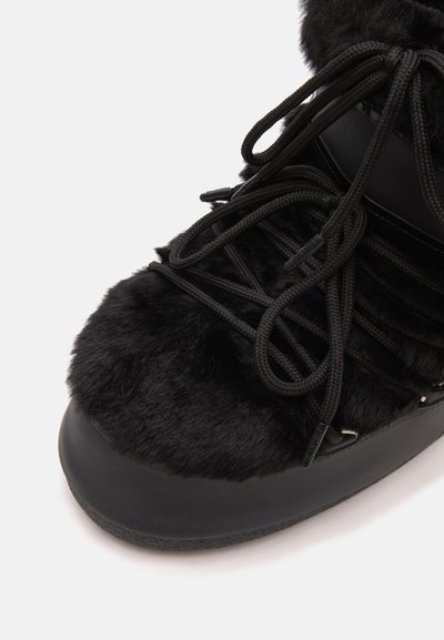 Gros plan d'une botte d'hiver noire avec une épaisse fourrure recouvrant la partie supérieure et des lacets ronds noirs noués sur le dessus.