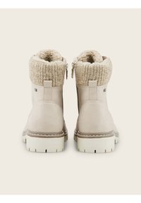 Bottines beiges avec revers en tricot, fermetures éclair latérales, doublure en polaire et semelles blanches épaisses, vues de dos sur un fond neutre.