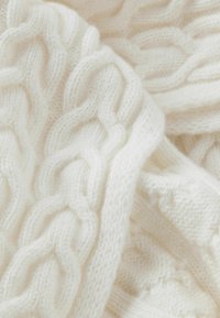 Hvid strikket sweater med et struktureret kabelmønster. Blødt, kraftigt garn skaber et hyggeligt udseende med synlige masker og ribstrikkede detaljer.