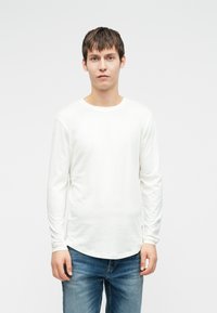 Λευκό πουκάμισο με μακριά μανίκια, φτιαγμένο από μαλακό ύφασμα, με στρογγυλή λαιμόκοψη και κυρτή ραφή, συνδυασμένο με μπλε τζιν. Απλός και χαλαρός σχεδιασμός.