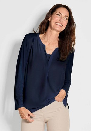 Blusa navy a maniche lunghe con scollatura tonda e cuciture sottili. Tessuto morbido con una vestibilità rilassata, abbinata a pantaloni beige chiaro.