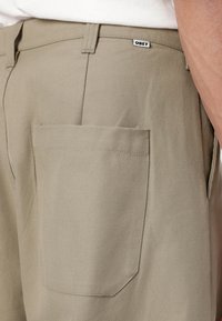 Khaki pants with a straight cut, made of sturdy fabric. Features a back pocket and an "OBEY" label near the waistband.