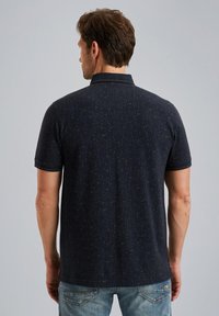 Camisa polo de color navy con mangas cortas, textura con patrón sutil, cuello clásico y detalle de costura distintivo. Llevada con jeans de color azul claro.