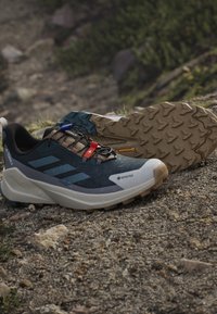 Outdoor hiking shoes with rugged soles, Gore-Tex material, and a blue, beige, and black color design resting on rocky terrain.