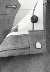 Gros plan sur le poignet d'une veste de costume grise montrant une boutonnière, une doublure intérieure blanche avec un bouton noir et un petit bouton de manchette en argent.