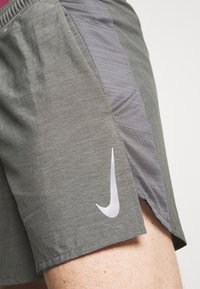 Shorts Nike en tissu gris foncé avec un panneau latéral texturé gris. Présente un logo Nike blanc sur l'ourlet et un design léger et respirant.