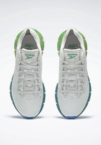 Baskets de sport blanches en mesh avec des accents verts et bleus, présentant une surface texturée, un design minimaliste et des lacets pour un ajustement sécurisé.